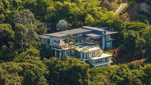 A modern multi-story house surrounded by dense greenery. - Casa Ombak 7-Bedroom Luxury Villa with Spa & Ocean View (Puntarenas Province)