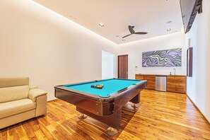 Ein modernes Zimmer mit Poolbillard, einer Couch, einem Deckenventilator und Wandkunst.