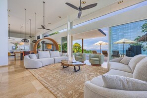 Ein großzügiger Wohnbereich mit einem großen Sofa, einem Couchtisch und Sesseln, Holzboden und Blick ins Freie.