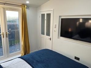 Een slaapkamer met een bed, een raam met gordijnen, een deur met geëtste glas en een aan de muur bevestigde televisie.