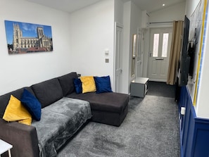 A modern living room with a sectional sofa, a flat-screen TV, and a painting of a cathedral. - House Sleeps 4 - Private Garden - Bbq (York)