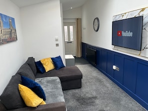 Een moderne woonkamer met een modulaire bank, een flatscreen televisie bevestigd aan een blauwe muur en een schilderij van een kathedraal.