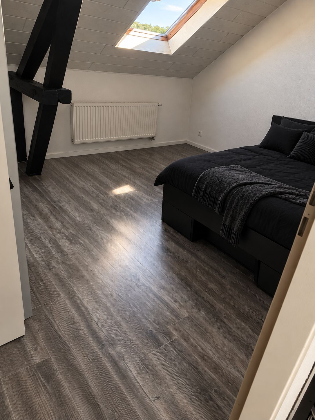 Ein Schlafzimmer mit schrägem Dach, einem Bett, einem Heizkörper und einem Dachfenster.