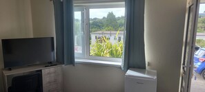 Een kamer met een televisie op een standaard, een klein wit apparaat en een raam met gordijnen.