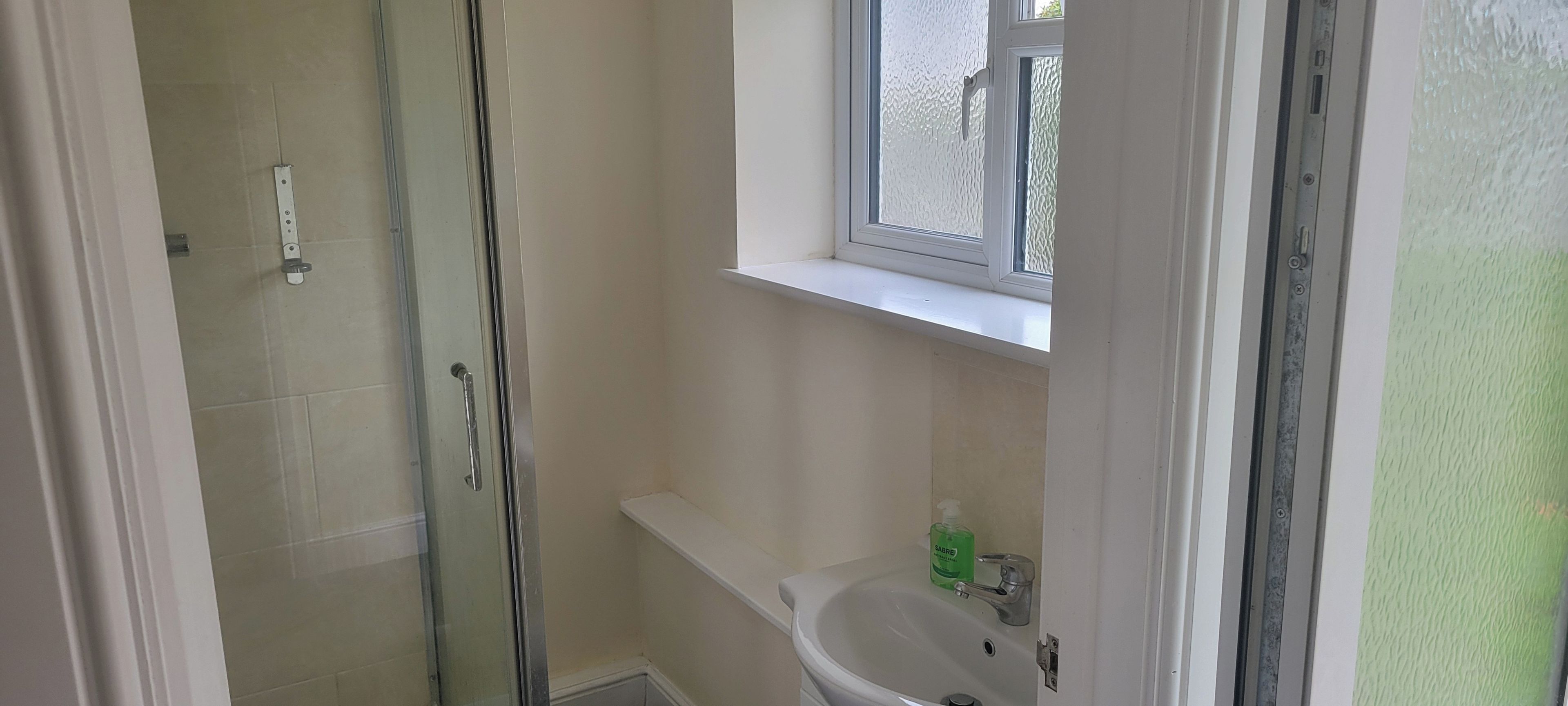 Un baño con cabina de ducha de vidrio, un lavabo y una ventana sobre el lavabo.