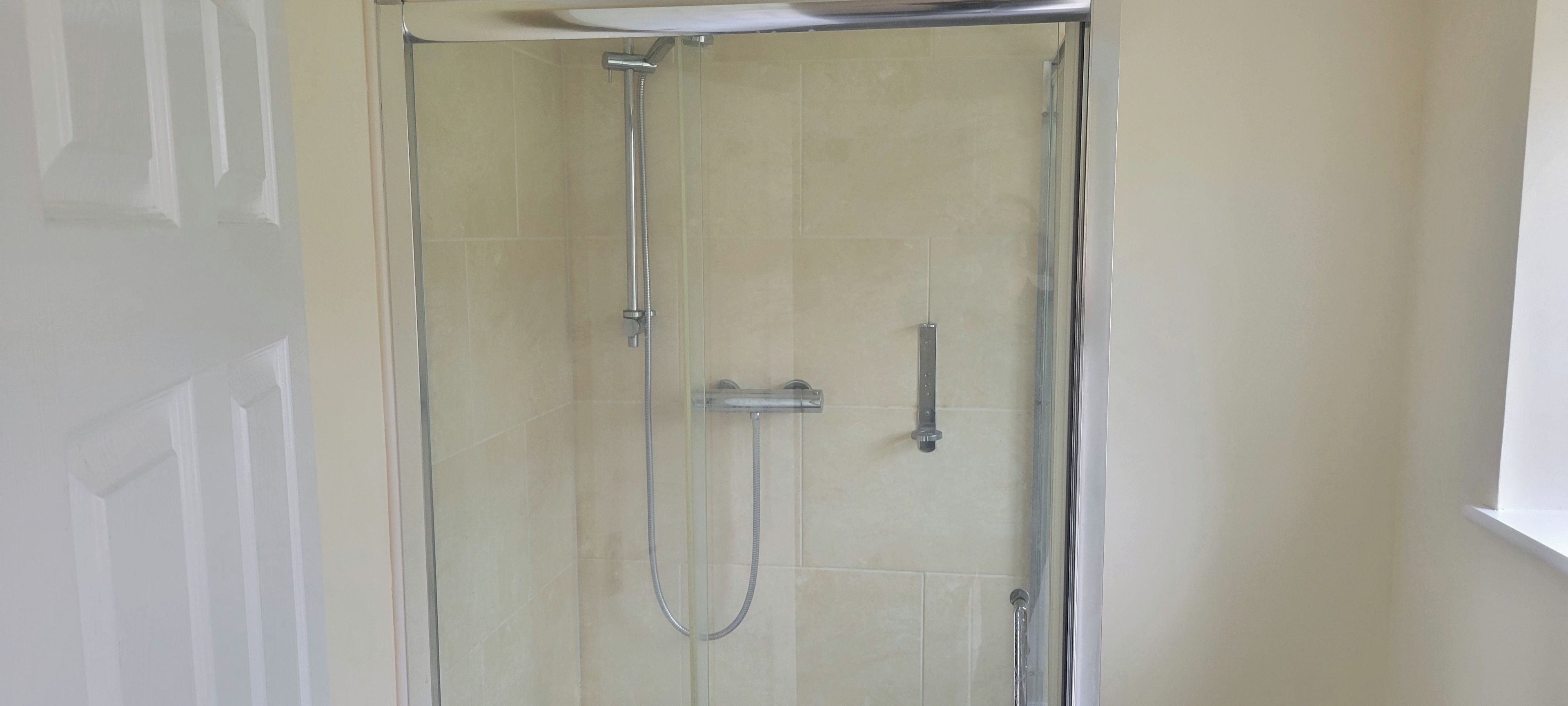 Een douchecabine met glazen wanden, een handdouche en een vastgeplakte kraan aan de muur.