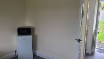 Une petite pièce avec un réfrigérateur blanc, un four à micro-ondes posé sur le dessus, et une porte donnant sur un espace extérieur verdoyant.
