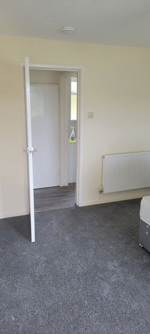 Ein Zimmer mit grauem Teppich, einem weißen Heizkörper und einer Tür zu einem anderen Raum.