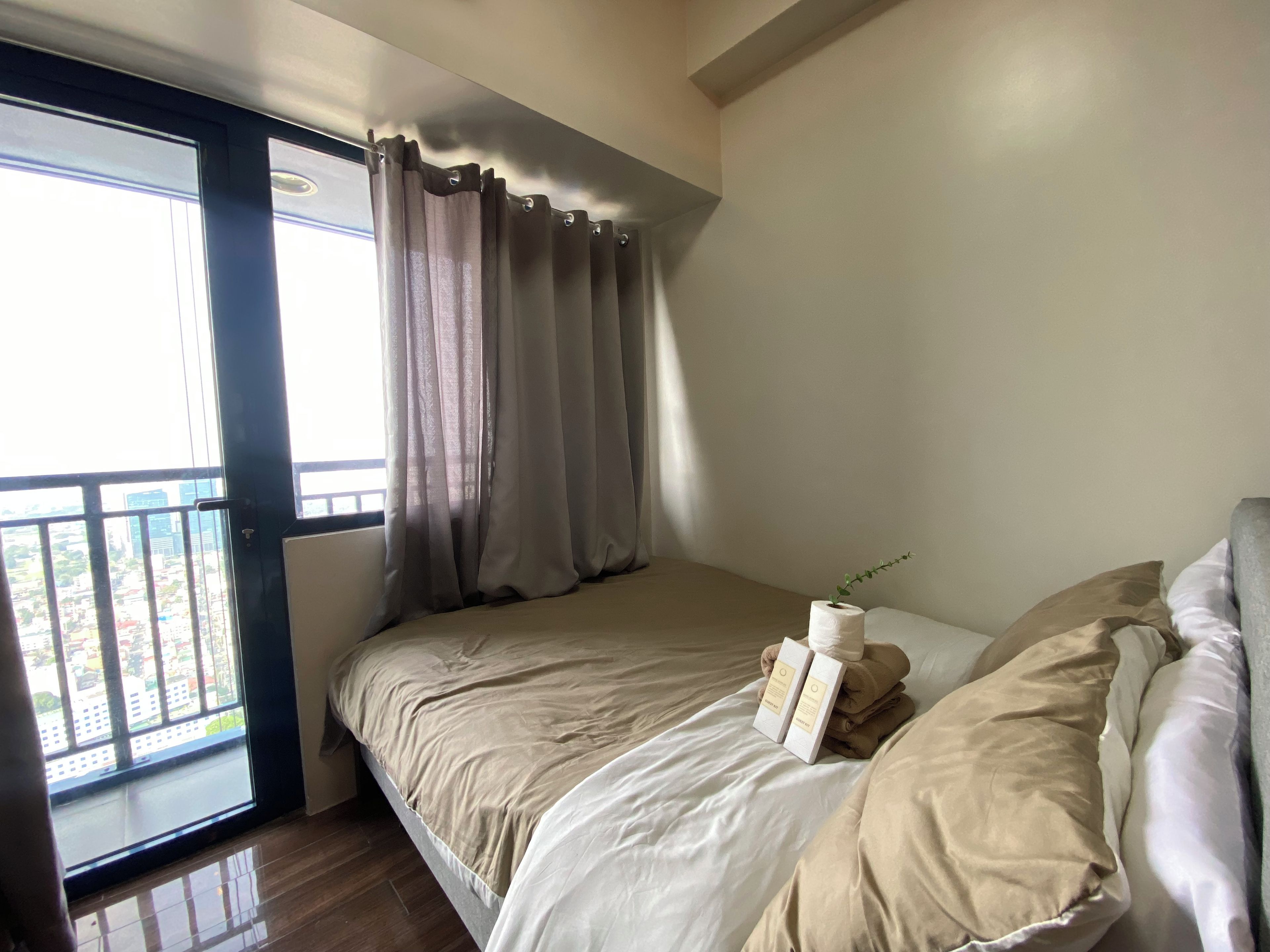 A bedroom with a bed, a window with curtains, and a view of the city.