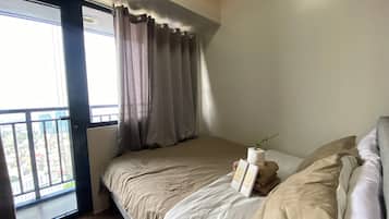 A bedroom with a bed, a window with curtains, and a view of the city.