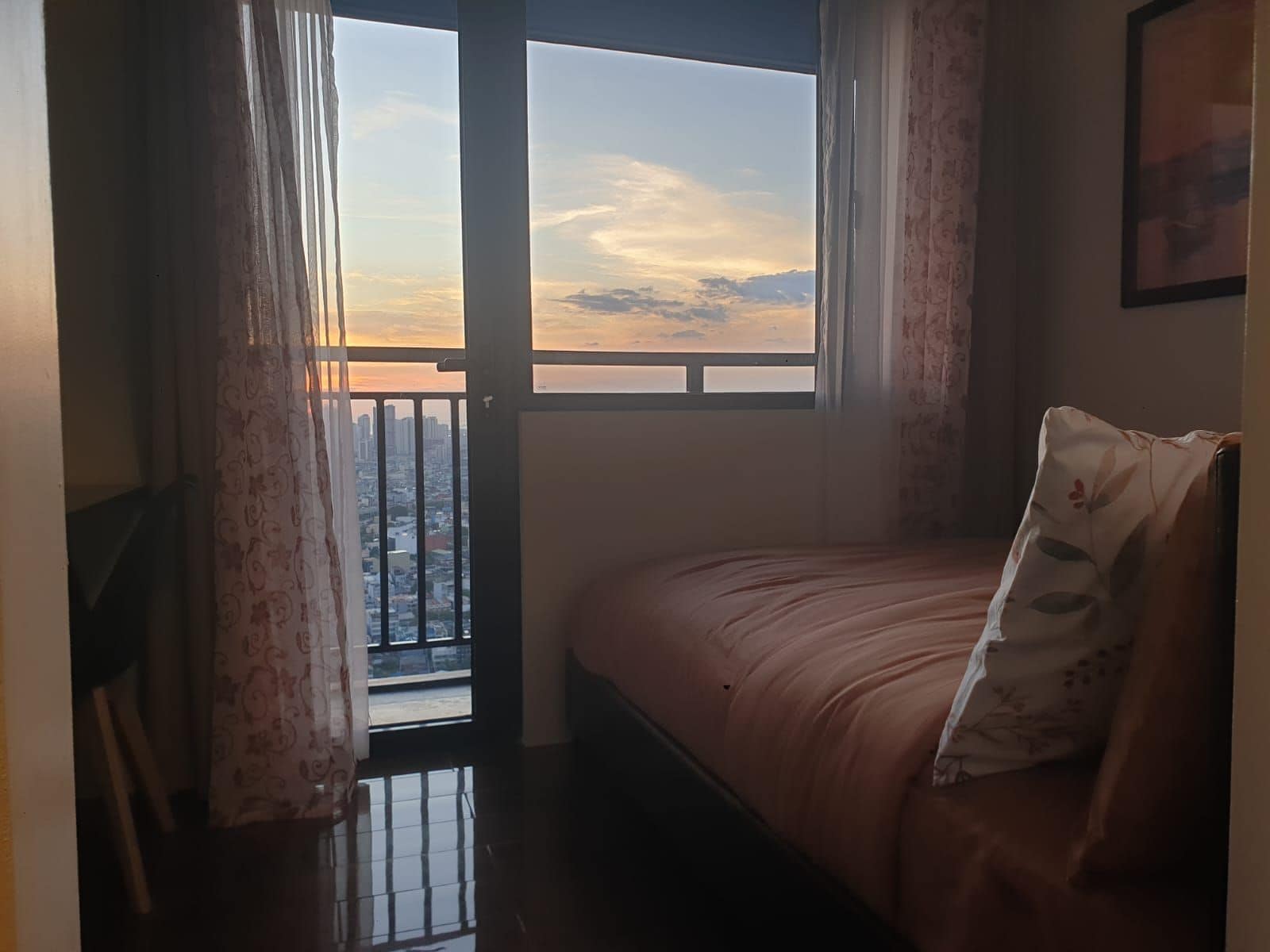 Ein Schlafzimmer mit einem Bett, einem Fenster mit Vorhängen und Blick auf eine Stadtlandschaft.