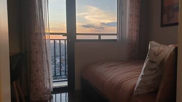 Ein Schlafzimmer mit einem Bett, einem Fenster mit Vorhängen und Blick auf eine Stadtlandschaft.