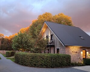 A brick building with a sloped roof, a balcony, and a pathway leading to it. - De Zandrug - Luxury vacation home and B&B with a hot tub and natural swimming pool surrounded by greenery (Stekene)
