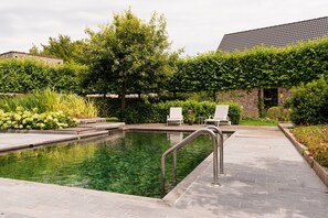 A swimming pool with a metal ladder, surrounded by a brick wall and greenery. - De Zandrug - Luxury vacation home and B&B with a hot tub and natural swimming pool surrounded by greenery (Stekene)