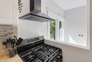 A modern kitchen with a gas stove, a range hood, and a window providing natural light. - Walk to Little Italy | 4BR | Sleeps 10 (San Diego)