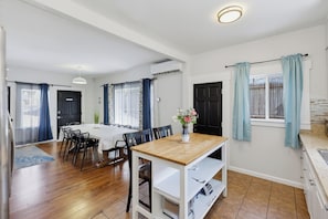 A dining area with a table and chairs, a kitchen with a sink, and a window with curtains. - Walk to Little Italy | 4BR | Sleeps 10 (San Diego)