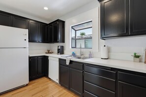 A modern kitchen with black cabinets, a white refrigerator, and a window above the sink. - Walk to Little Italy | 4BR | Sleeps 8 (San Diego)