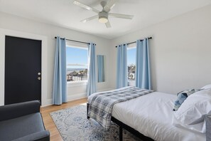 Ein Schlafzimmer mit Bett, Stuhl, Deckenventilator und Blick auf die Stadt durch das Fenster.