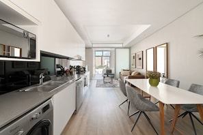 Eine moderne Küche mit Geschirrspüler, ein Essbereich mit Tisch und Stühlen sowie ein Blick auf die Stadt durch große Fenster.