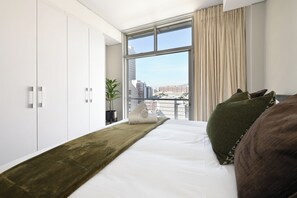 A modern hotel room with a large bed, a view of the city through a window, and a balcony. - Scenic 1BR Retreat Mountain & City Views in vibrant Cape Town (Cape Town)