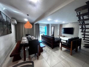 A modern living room with a dining area, a flat-screen TV mounted on the wall, and a bench. - Cj21MSII-3D Porto Seguro - Piscinas/Sauna/Conforto (Porto Seguro)