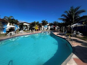 Una piscina con lettini e ombrelloni, circondata da palme e edifici.