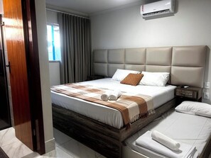 A hotel room with a bed, a nightstand, an air conditioning unit, and a window with curtains. - Cj21MSII-3D Porto Seguro - Piscinas/Sauna/Conforto (Porto Seguro)