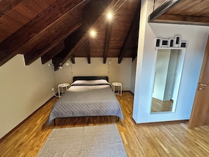A bedroom with a wooden ceiling, a bed with a grey quilt, two bedside tables, and a mirror on the wall.