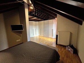 Un dormitorio con cama, televisión, radiador y una escalera que lleva a otra habitación.