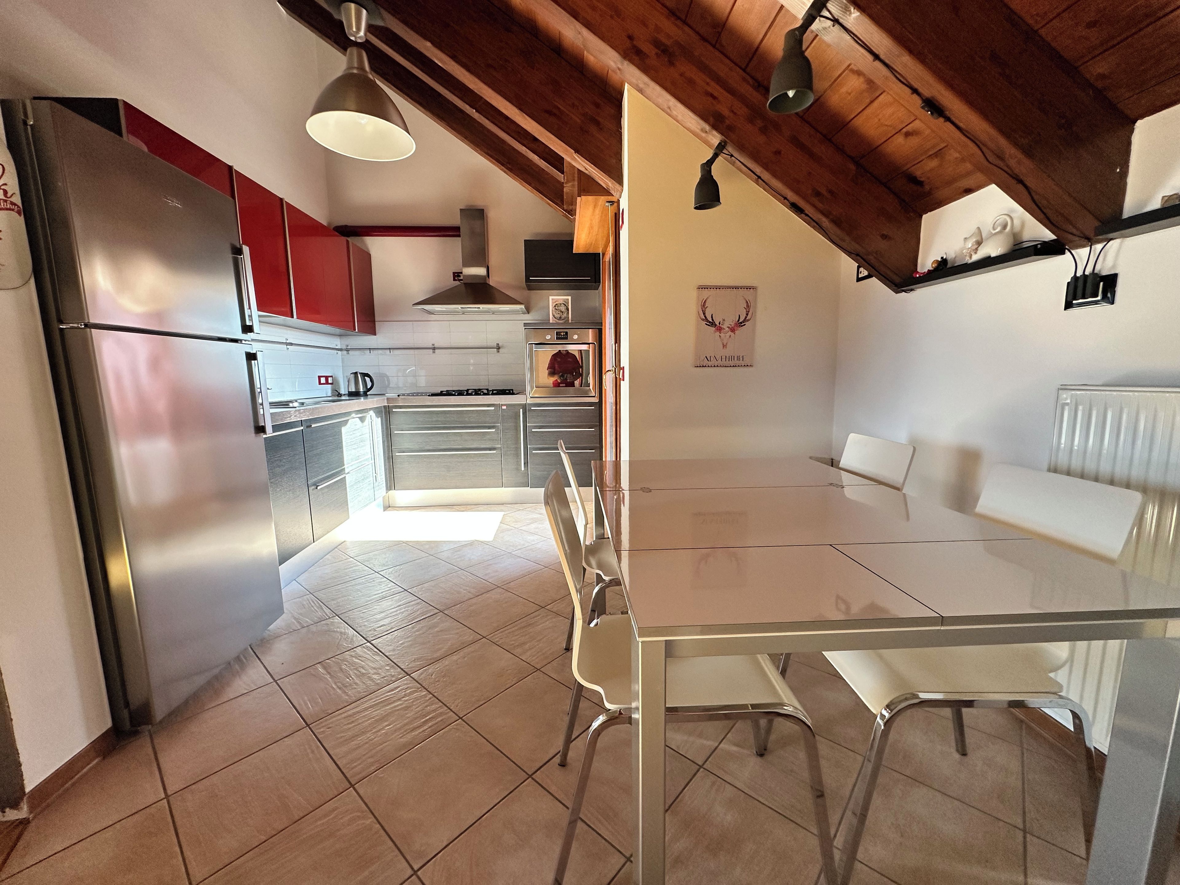 Une cuisine moderne dotée d’appareils électroménagers en acier inoxydable, un coin repas avec une table en verre et un plafond en bois.