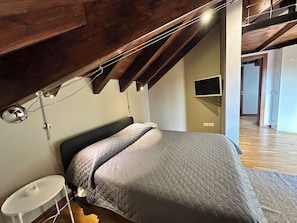 Een slaapkamer met een bed, nachtkastje, lamp en een televisie aan de muur.