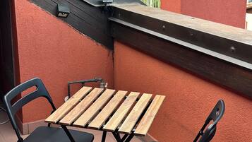 Un petit espace extérieur aménagé avec une table en bois et deux chaises, offrant une vue sur un quartier résidentiel avec des maisons et des montagnes à l’horizon.