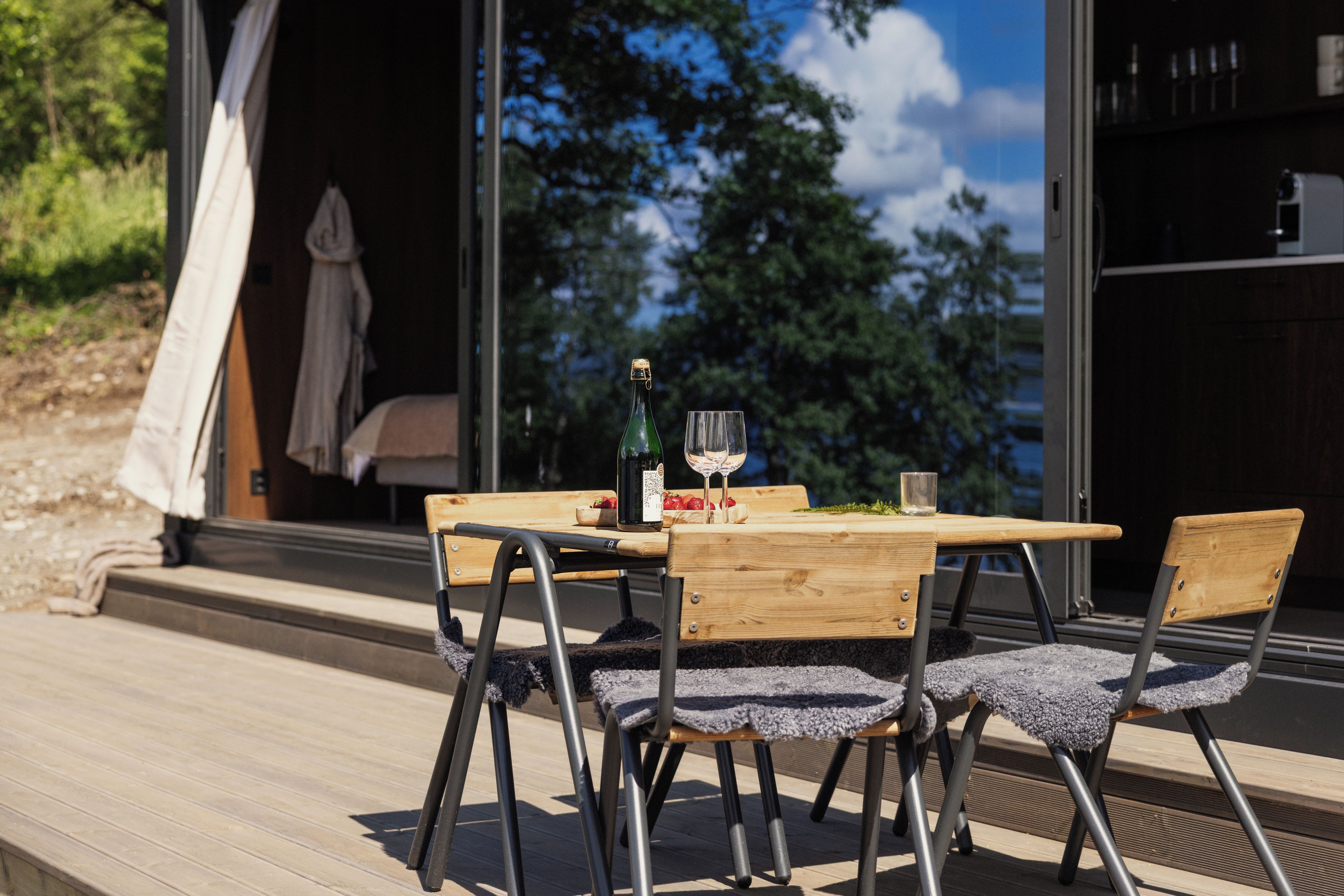 Una terraza exterior de madera con una mesa, sillas, una botella de vino y una copa.