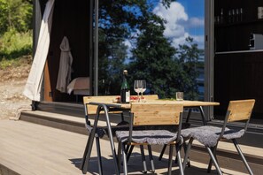Eine Terrasse aus Holz mit Tisch, Stühlen, einer Weinflasche und einem Glas.
