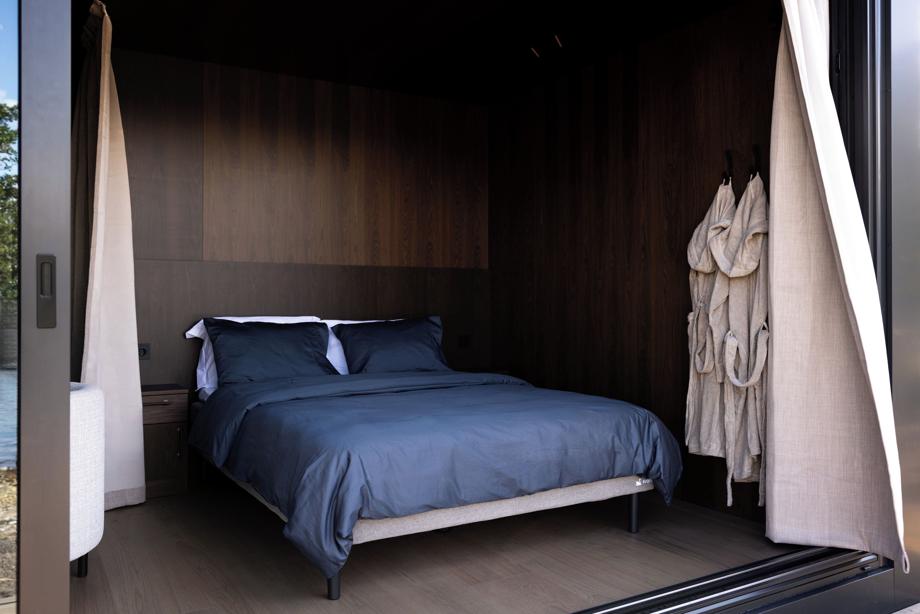 Een moderne slaapkamer met een bed, een nachtkastje en een badjas hangend aan een deur.