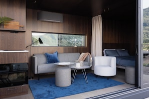 Ein modernes Wohnzimmer mit Sofa, Sessel, Couchtisch und einem großen Fenster mit Blick.