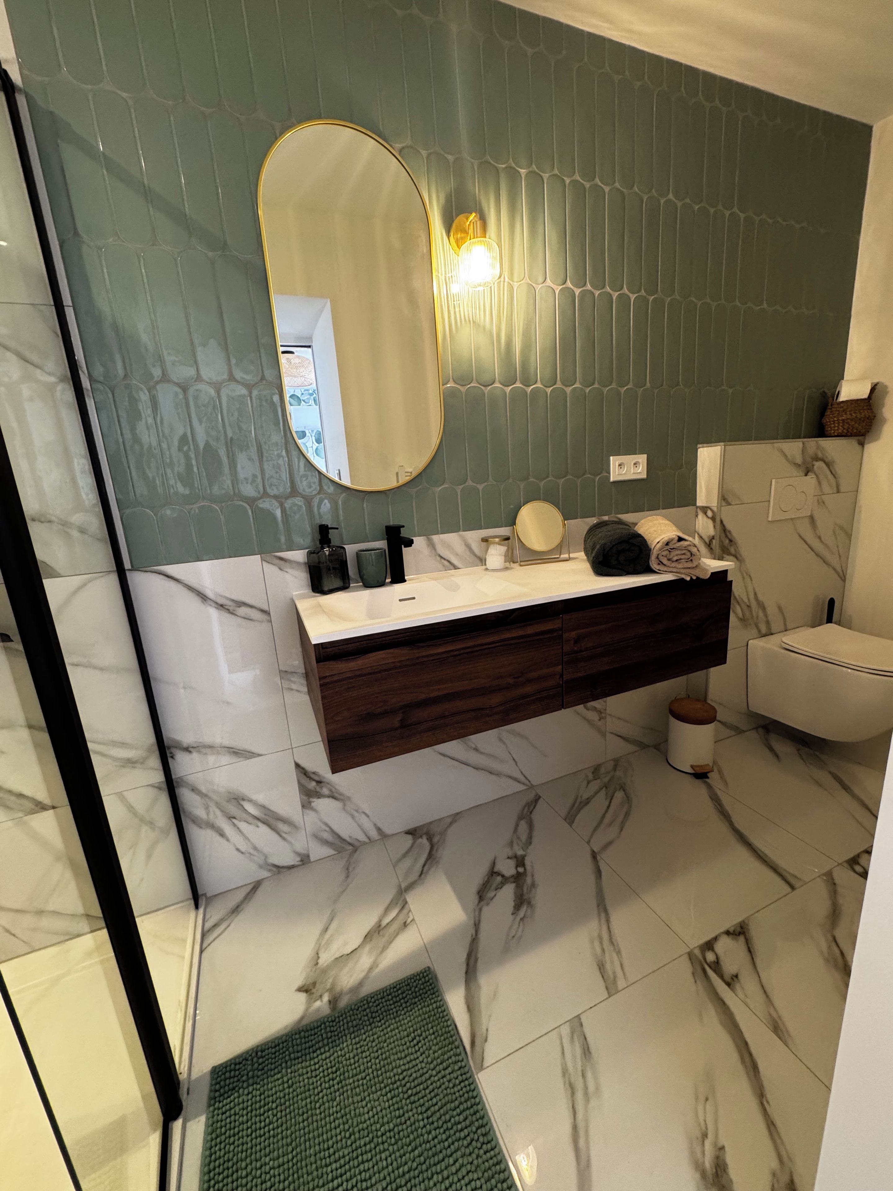 Un baño con piso de mármol, tocador de madera, espejo redondo y pared verde.