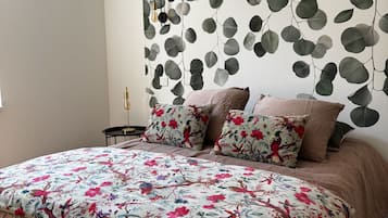 A bedroom with a bed, floral bedding, a wall-mounted air conditioner, and a wall with a leafy pattern.