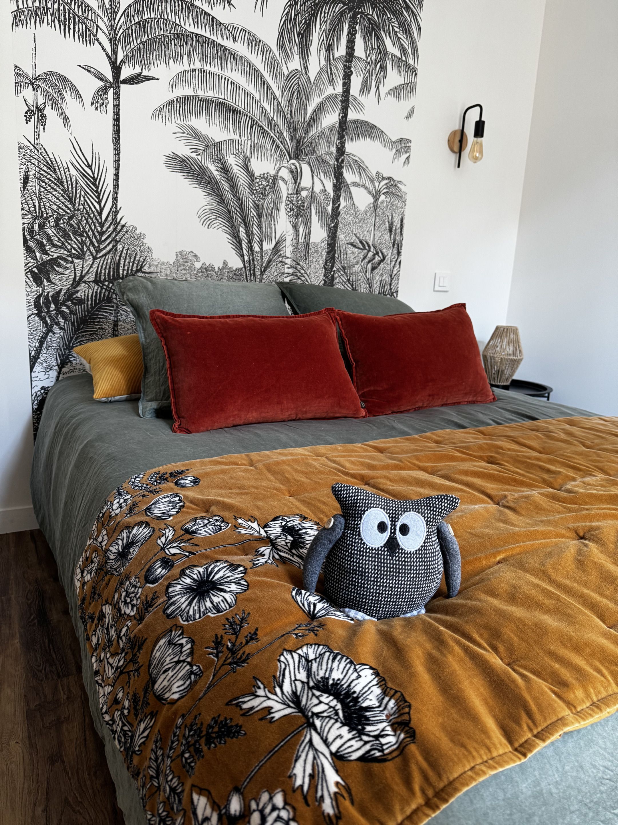 Un dormitorio con cama, almohadas, una colcha y un mural en la pared.