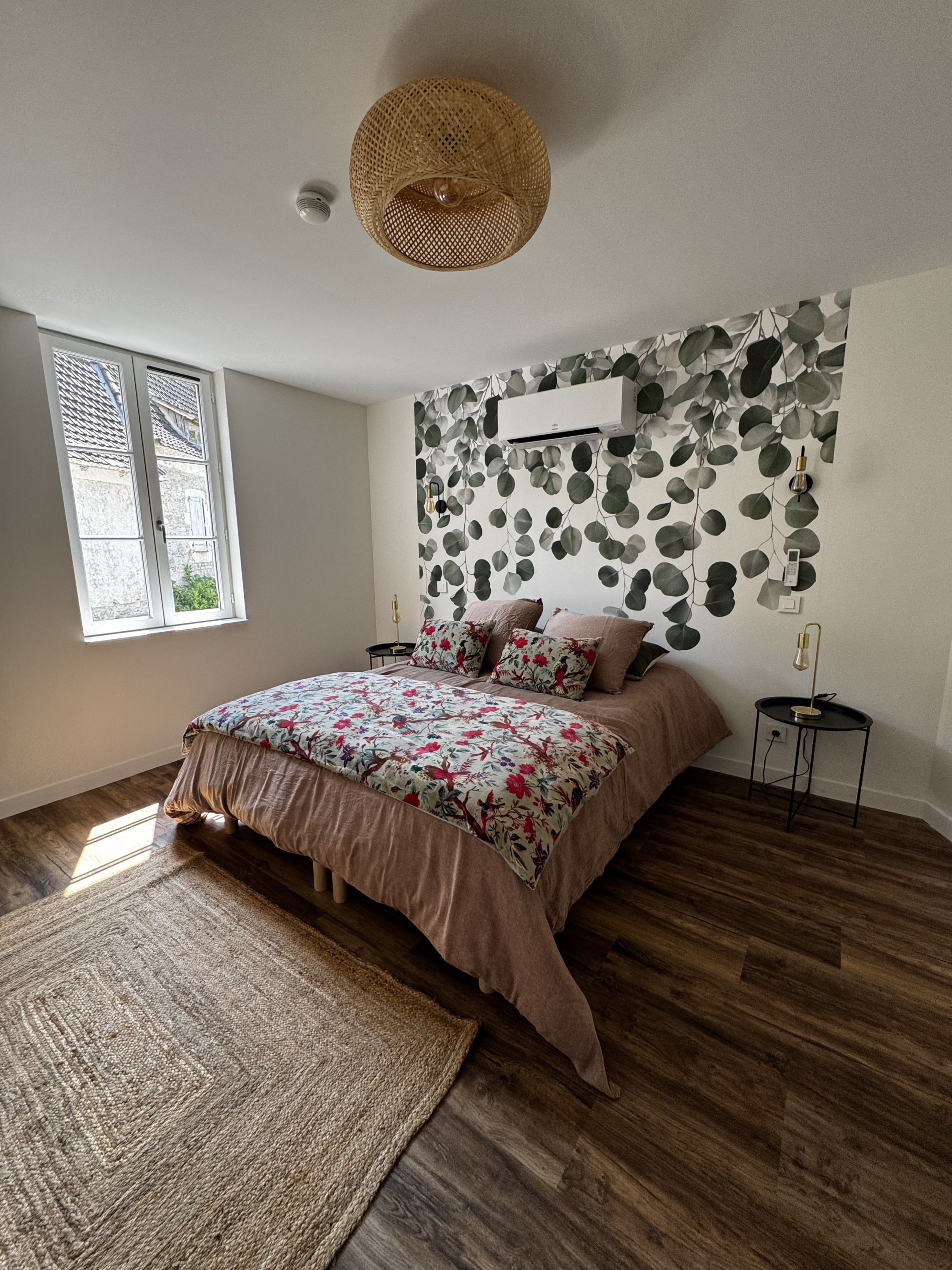 A bedroom with a bed, a large window, a wall-mounted air conditioner, and a woven ceiling light fixture.