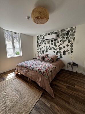 A bedroom with a bed, a large window, a wall-mounted air conditioner, and a woven ceiling light fixture.