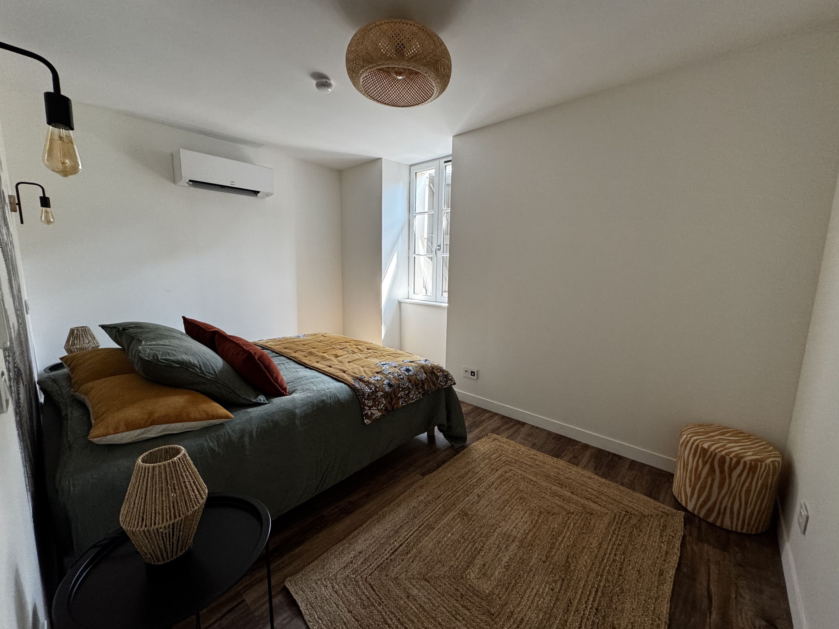 Une chambre à coucher avec un lit, une fenêtre, un luminaire suspendu et un climatiseur fixé au mur.
