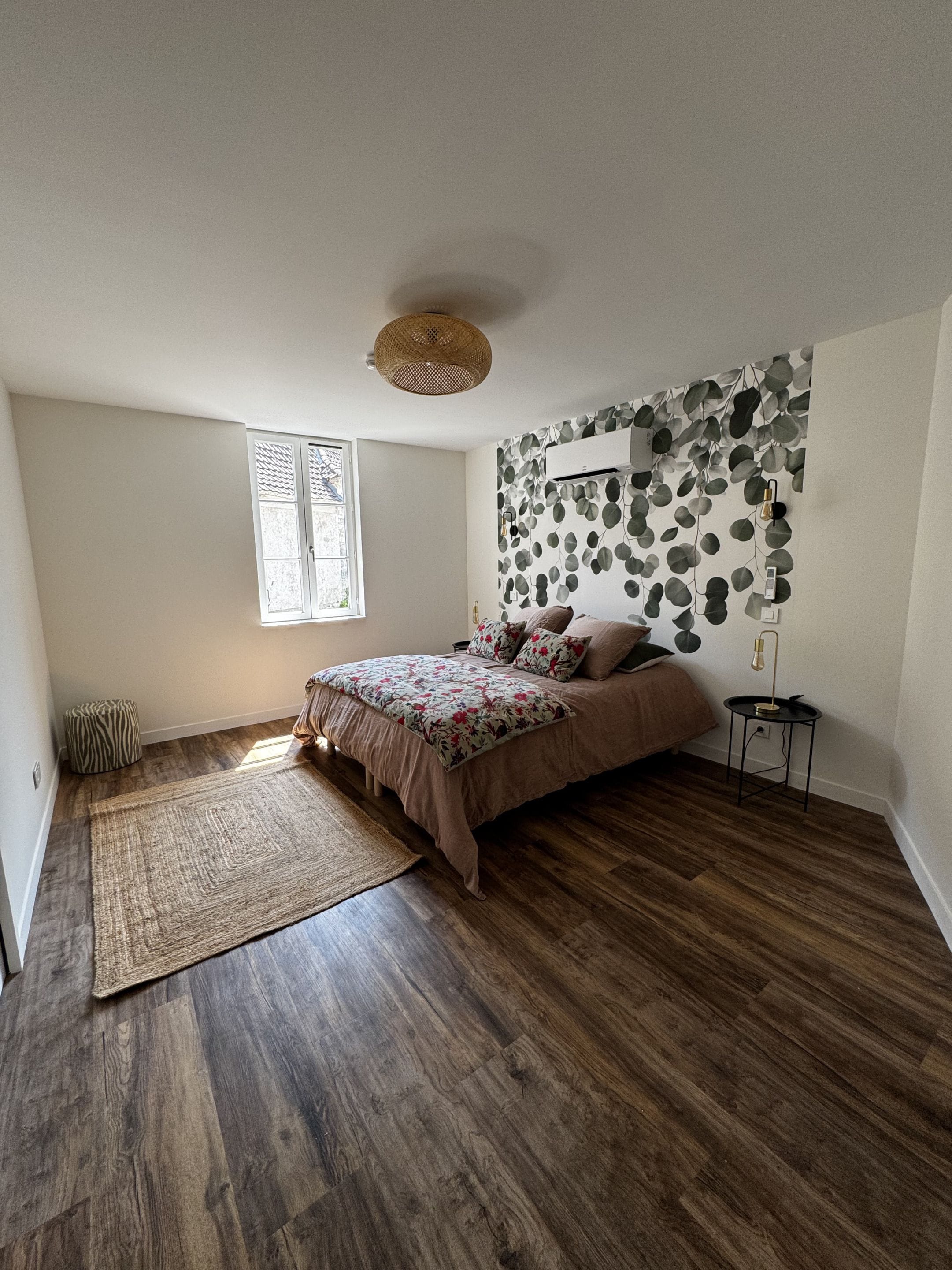A bedroom with a bed, a window, a wall-mounted air conditioner, and a floor lamp.