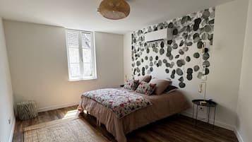 A bedroom with a bed, a window, a wall-mounted air conditioner, and a floor lamp.