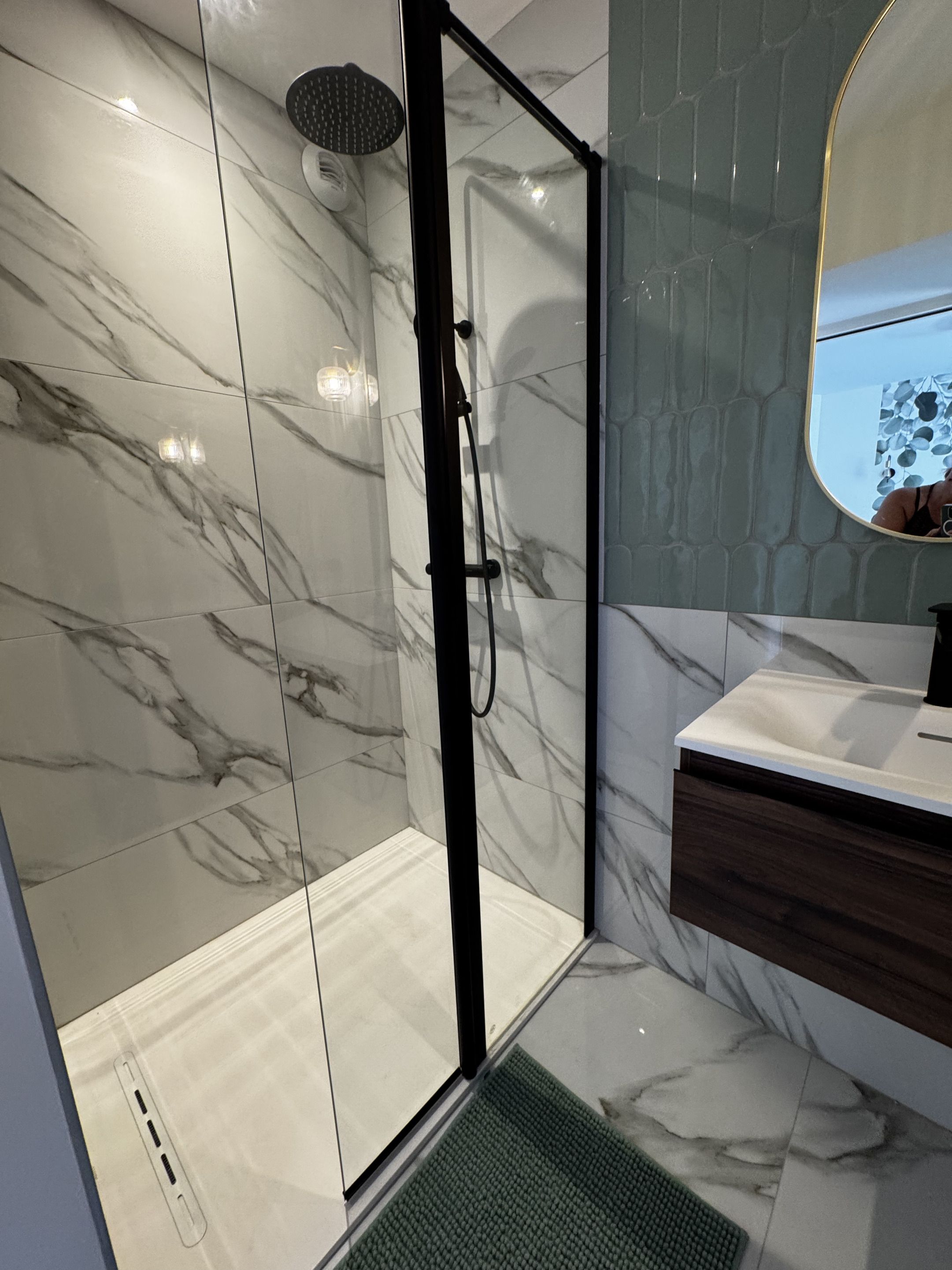 Un bagno moderno con box doccia in vetro, parete rivestita in marmo e mobile lavabo in legno.