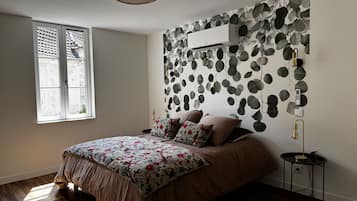 A bedroom with a bed, a window, a wall-mounted air conditioner, and a small bedside table.