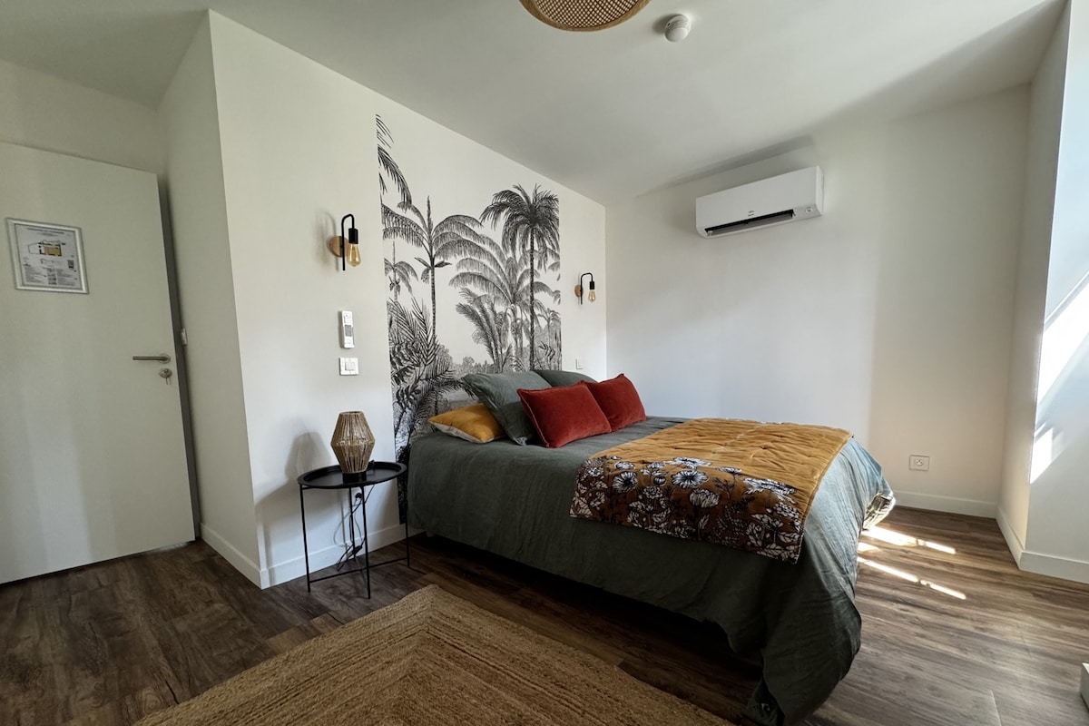 A bedroom with a bed, a wall-mounted air conditioner, a small table with a lamp, and a patterned throw blanket.