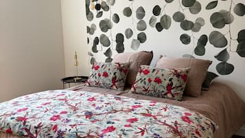 A bedroom with a bed, pillows, a wall-mounted air conditioner, and a wall with a leaf pattern.