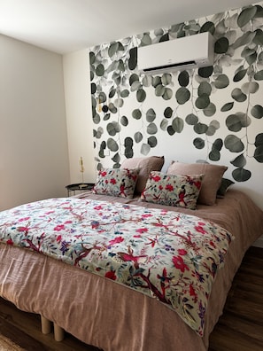 A bedroom with a bed, pillows, a wall-mounted air conditioner, and a wall with a leaf pattern.