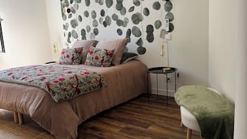 Un dormitorio con cama, aire acondicionado de pared, mesita de noche con lámpara y un banco con manta.